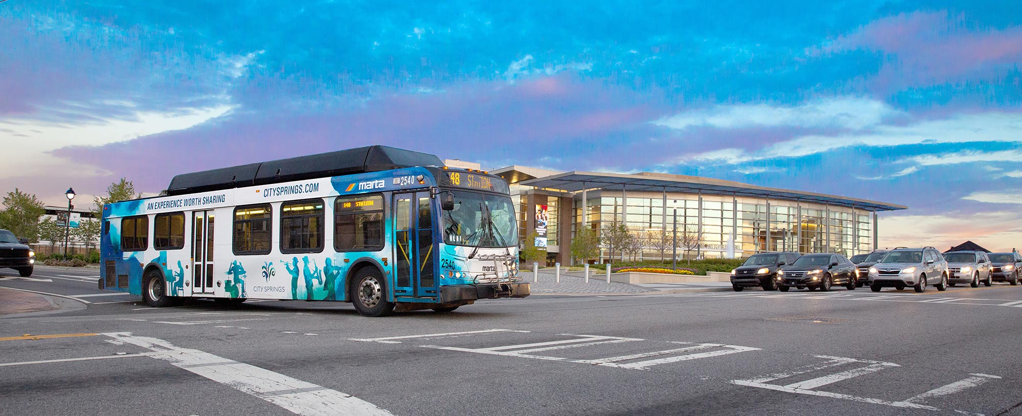 A MARTA Bus turns the corner on Mt. Vernon Hwy - It is wrapped in a City Springs design; blue and white watercolors feature silhouettes of people playing musical instruments